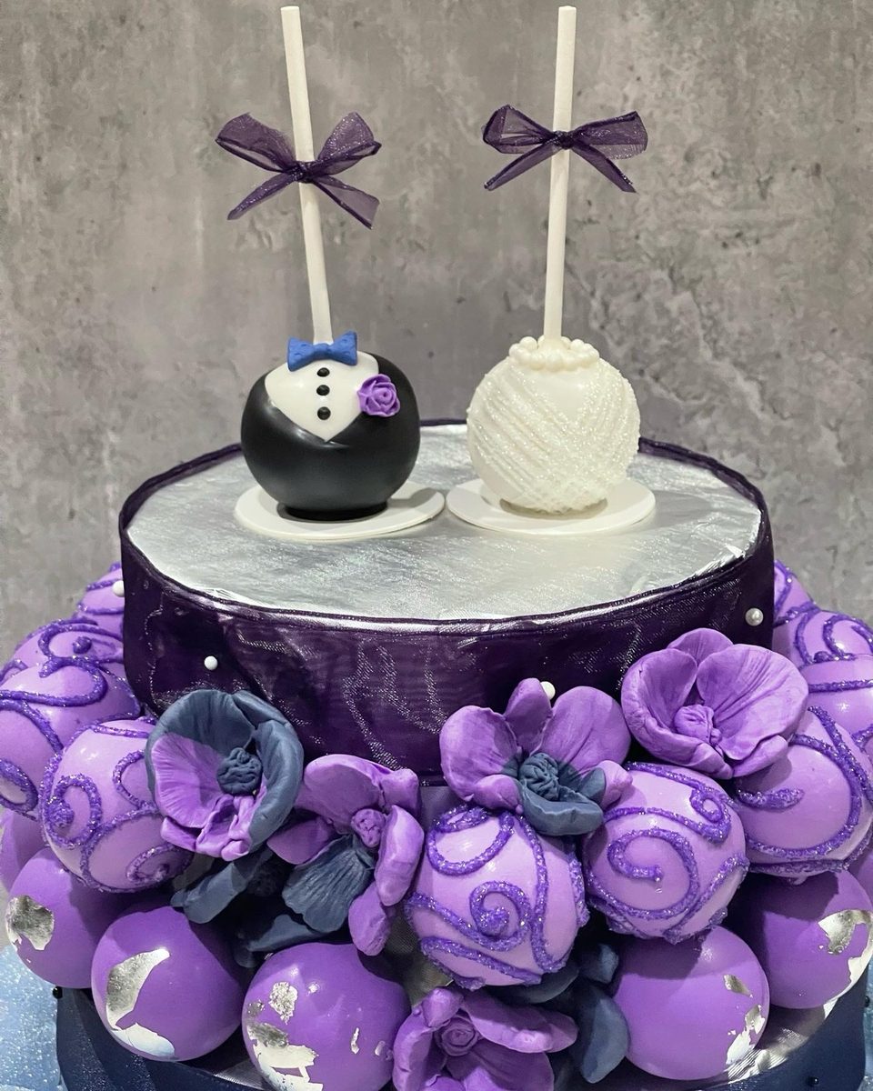 Bride and groom cake pops atop a tier of purple cake pops with sugar flowers